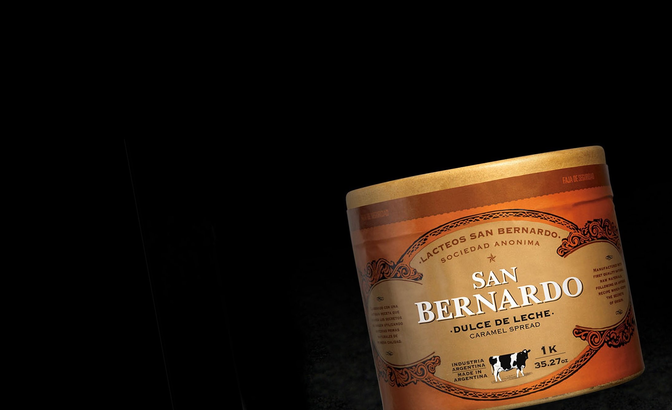 Una lata marrón etiquetada "San Bernardo Dulce de Leche Caramel Spread" con un diseño ornamentado está centrada contra un fondo oscuro, dando una sensación rústica y premium.