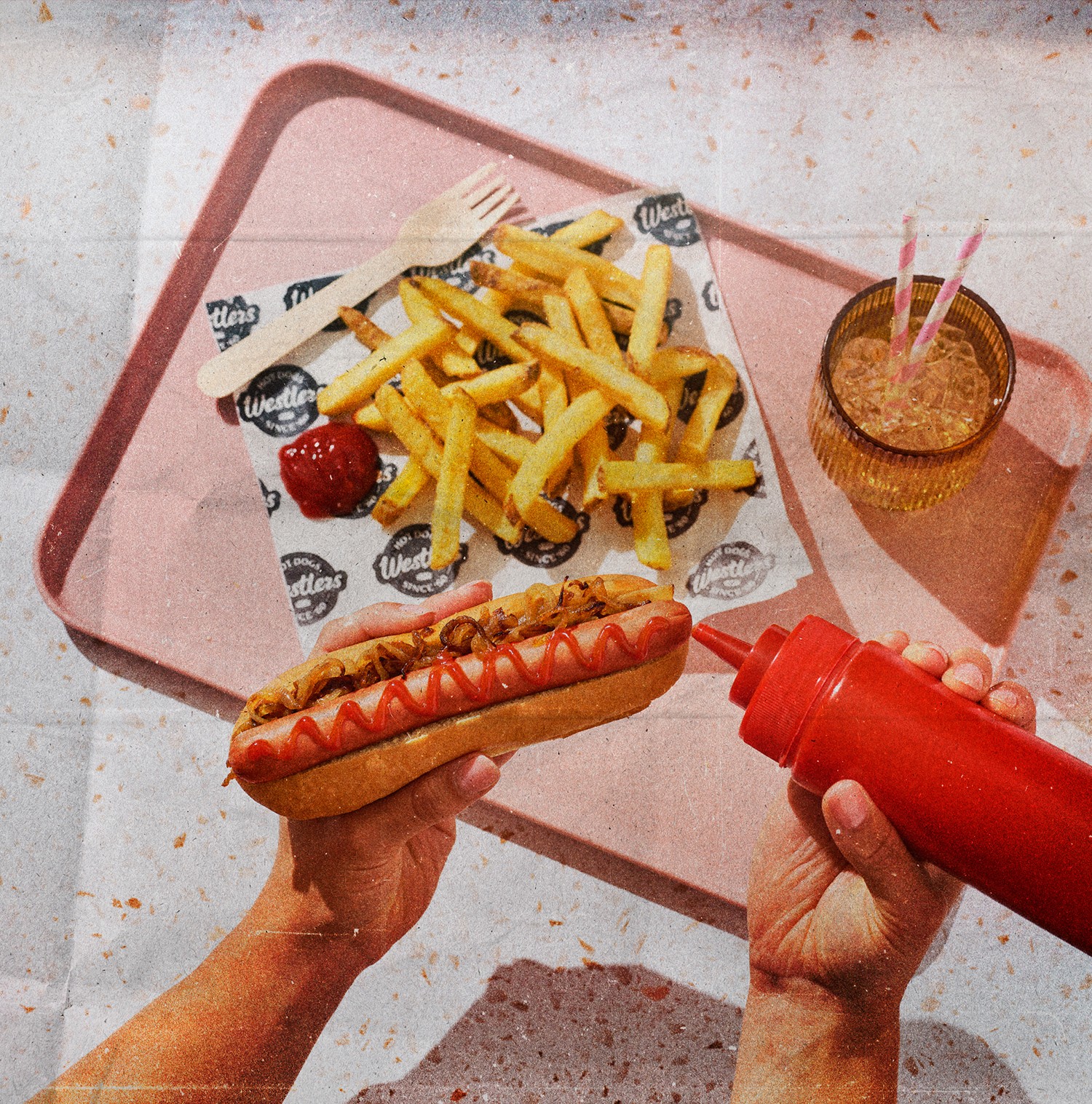 Scene showing hotdog, fries and hand squeezing ketchup on hotdog