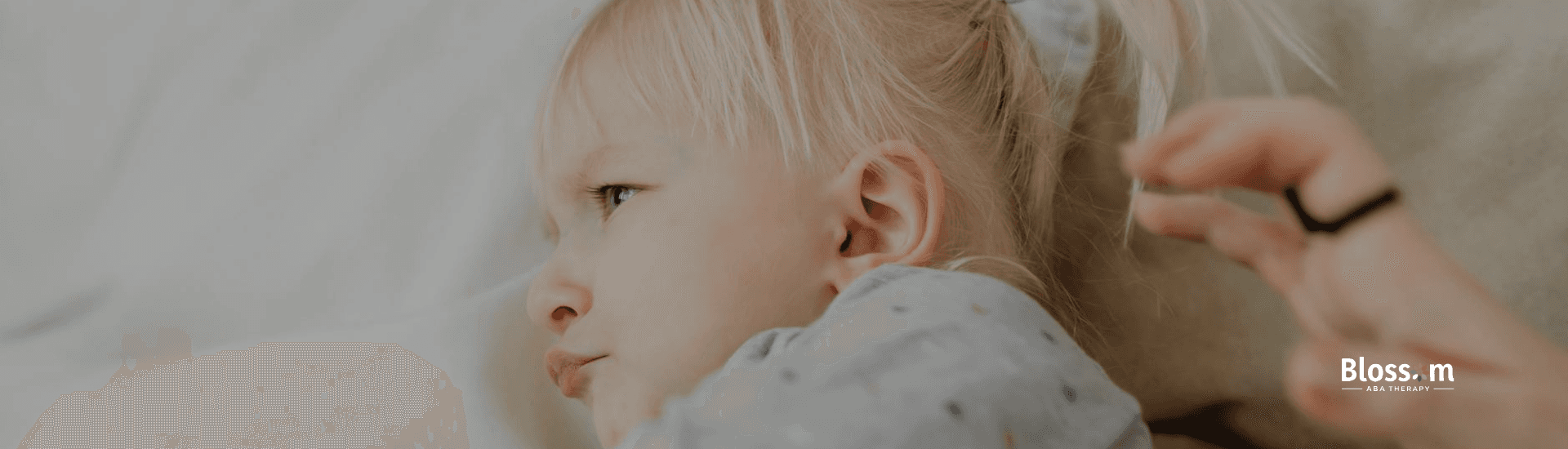 Girl with autism lying with her hair tied in a ponytail, looking upset & showing autistic shutdown.