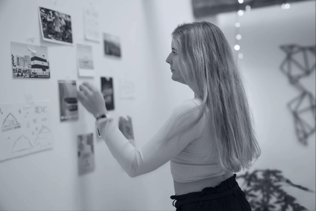 A black and white image of a guy talking to someone sitting with his back towards the camera and an open laptop in front of him 