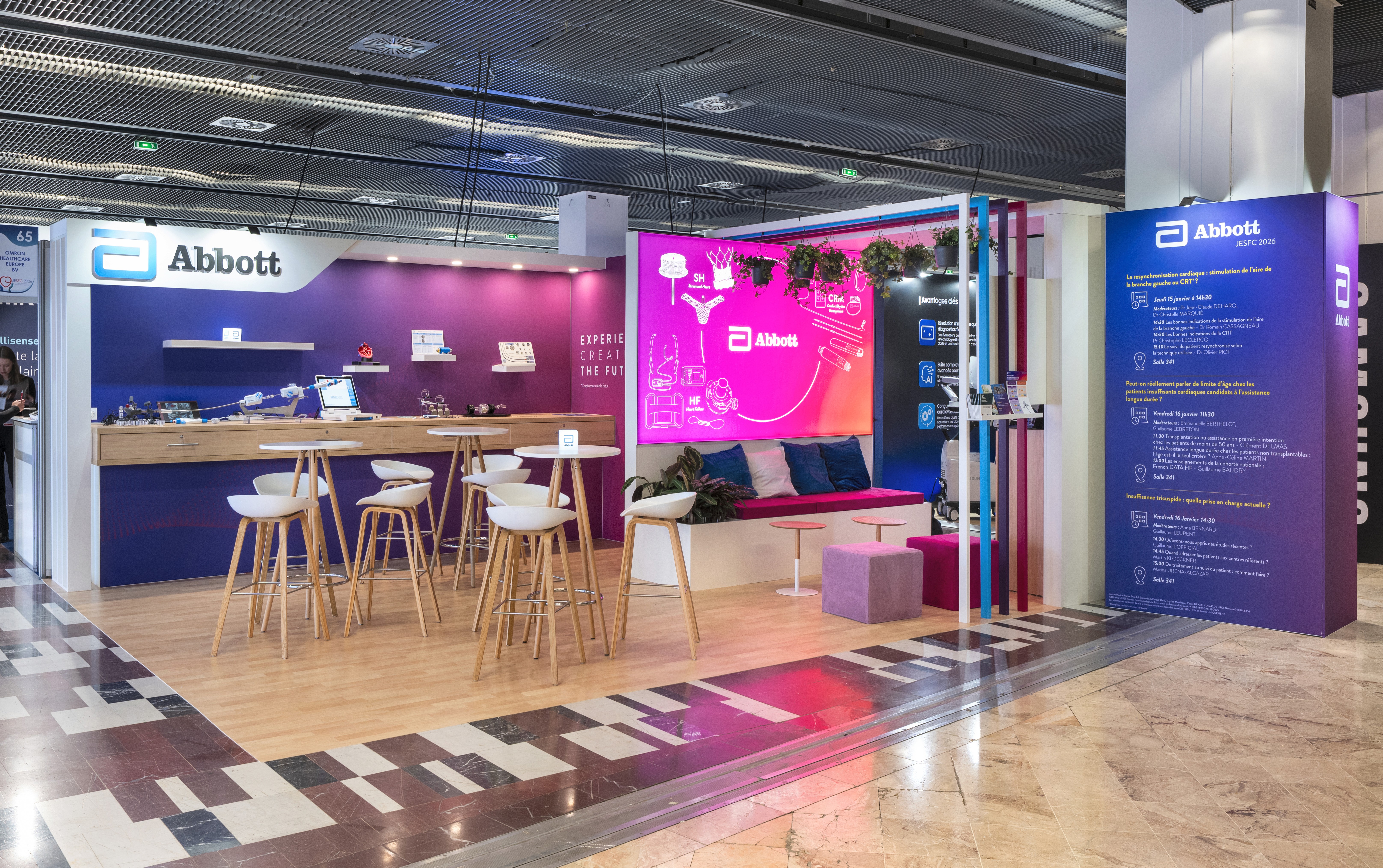 Stand Abbott JESFC 2026 par Expace – vue frontale avec logo Abbott, espace tables hautes bois et blanc, écran LED cardiologie et totem programme scientifique violet