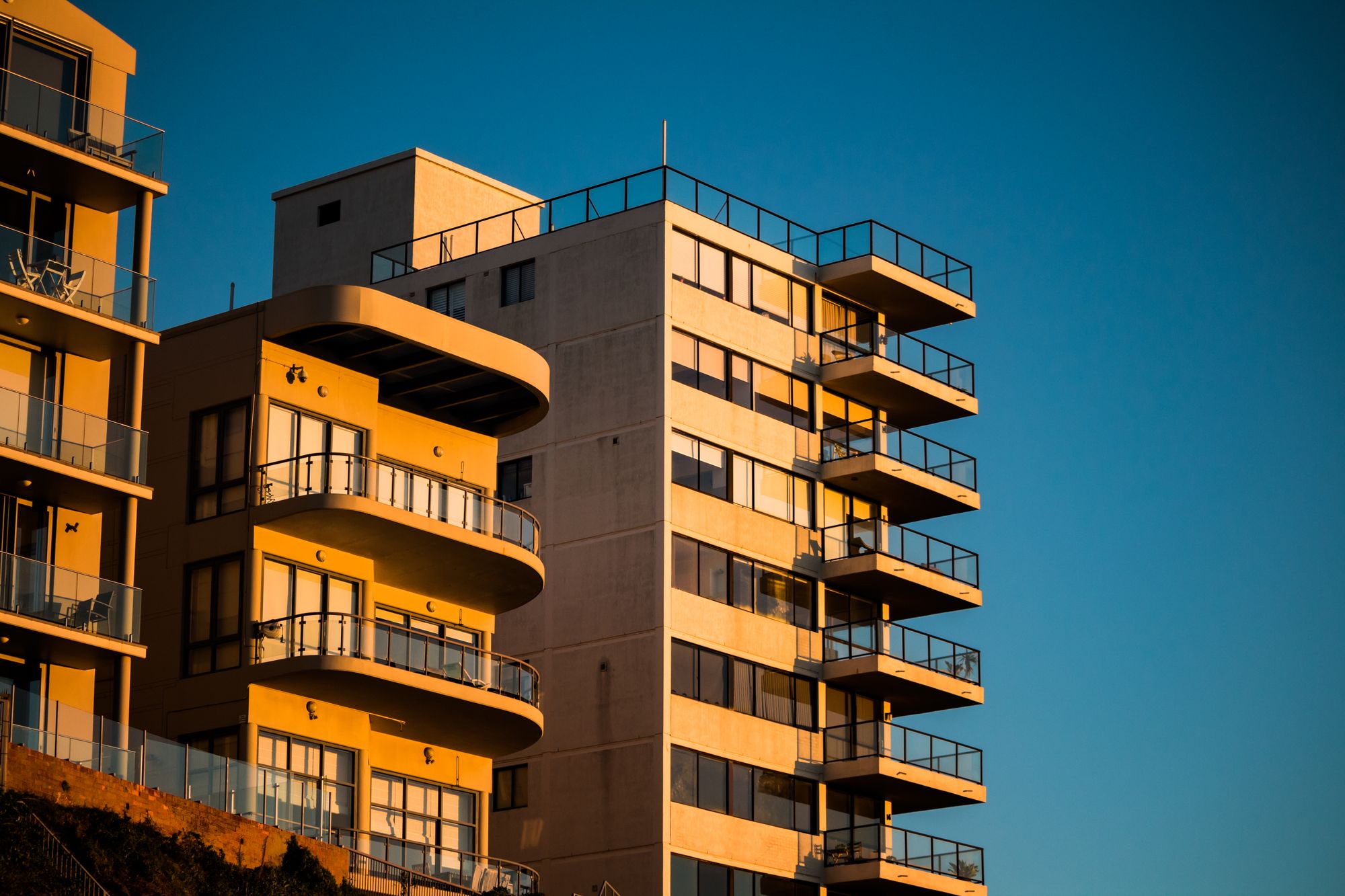 Apartment buildings with deep balconies, lit by low evening sun against a blue sky