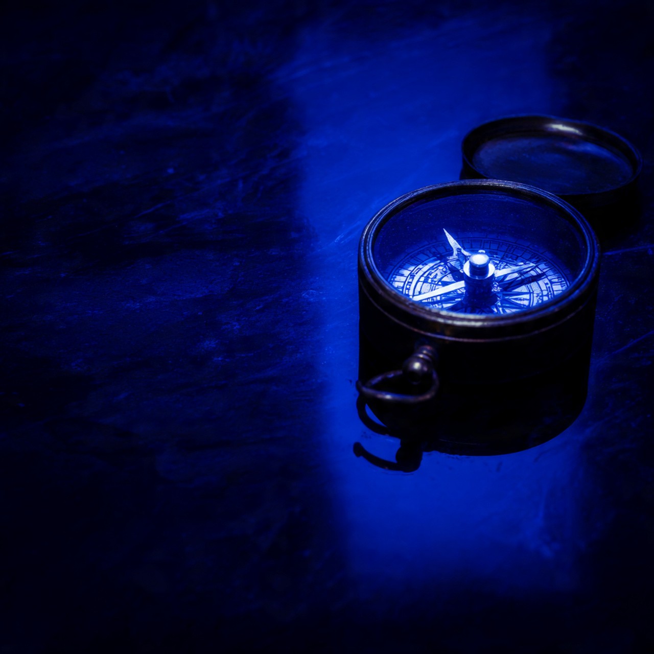 Close-up of a compass with its lid open, set against a dark blue surface, showing the directional needle.