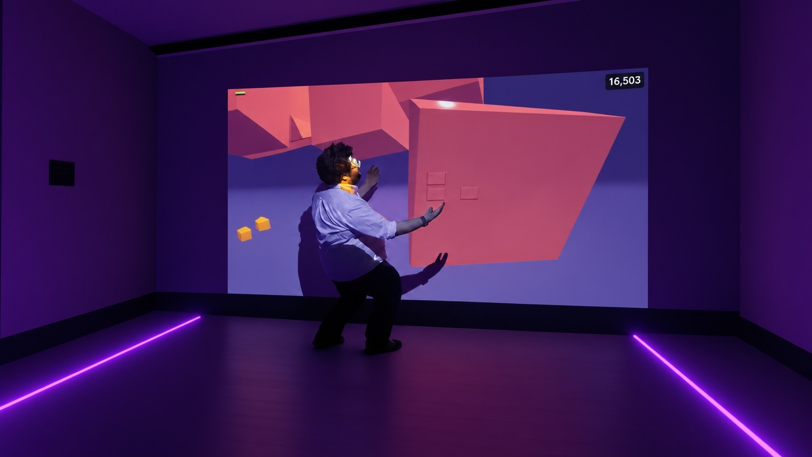 A person reaching toward pink shapes projected on the wall of The Byte Room