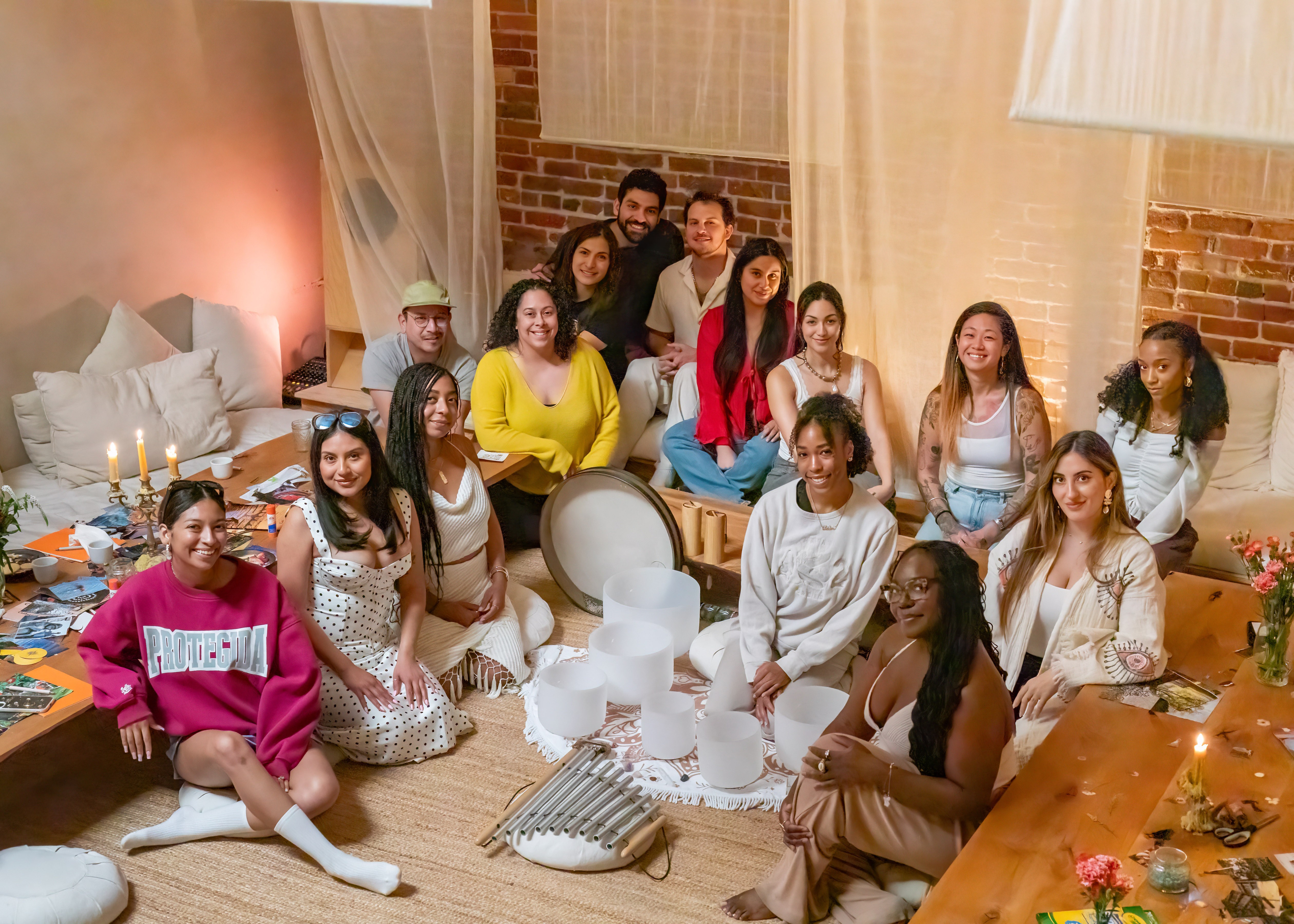 A group of peopl sitting in a room with white pillows and wooden tables around sound bowls smiling