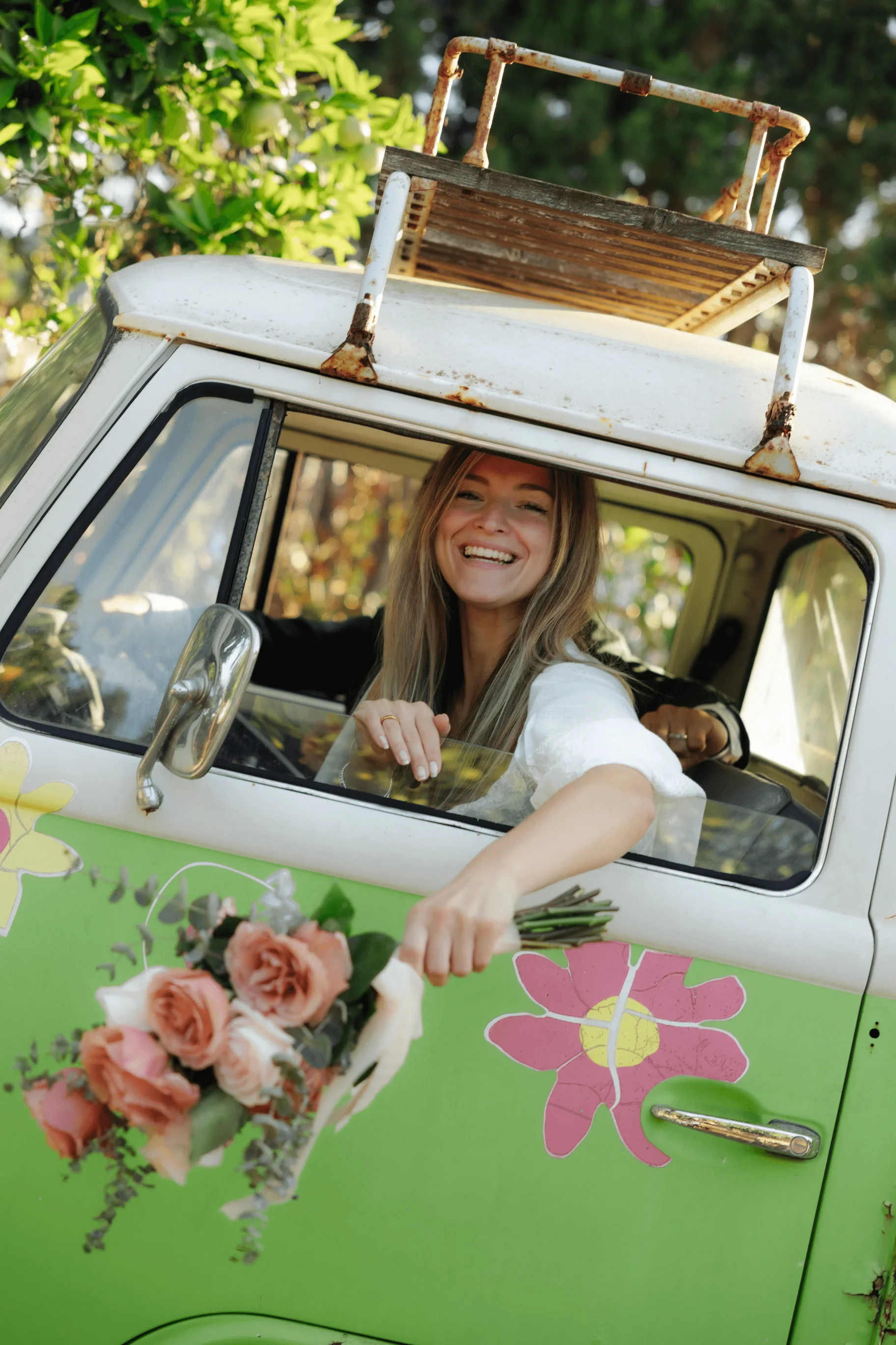 Smiling woman in VW bus holds bouquet.