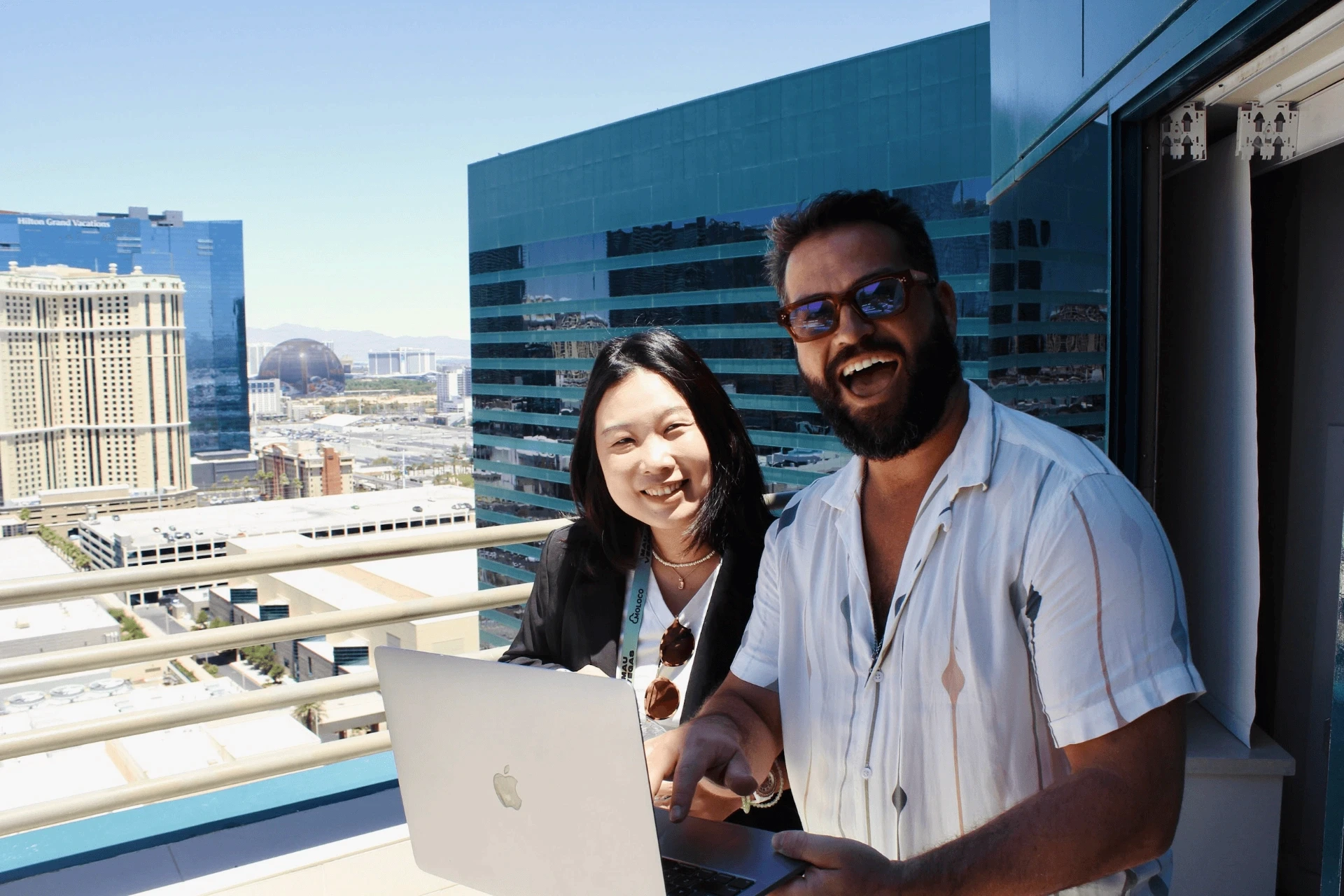 Smiling man and woman discuss offerwall on laptop from a Las Vegas balcony.