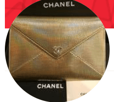 The image shows a gold-toned Chanel envelope clutch with a textured, metallic finish and the iconic logo on the front.