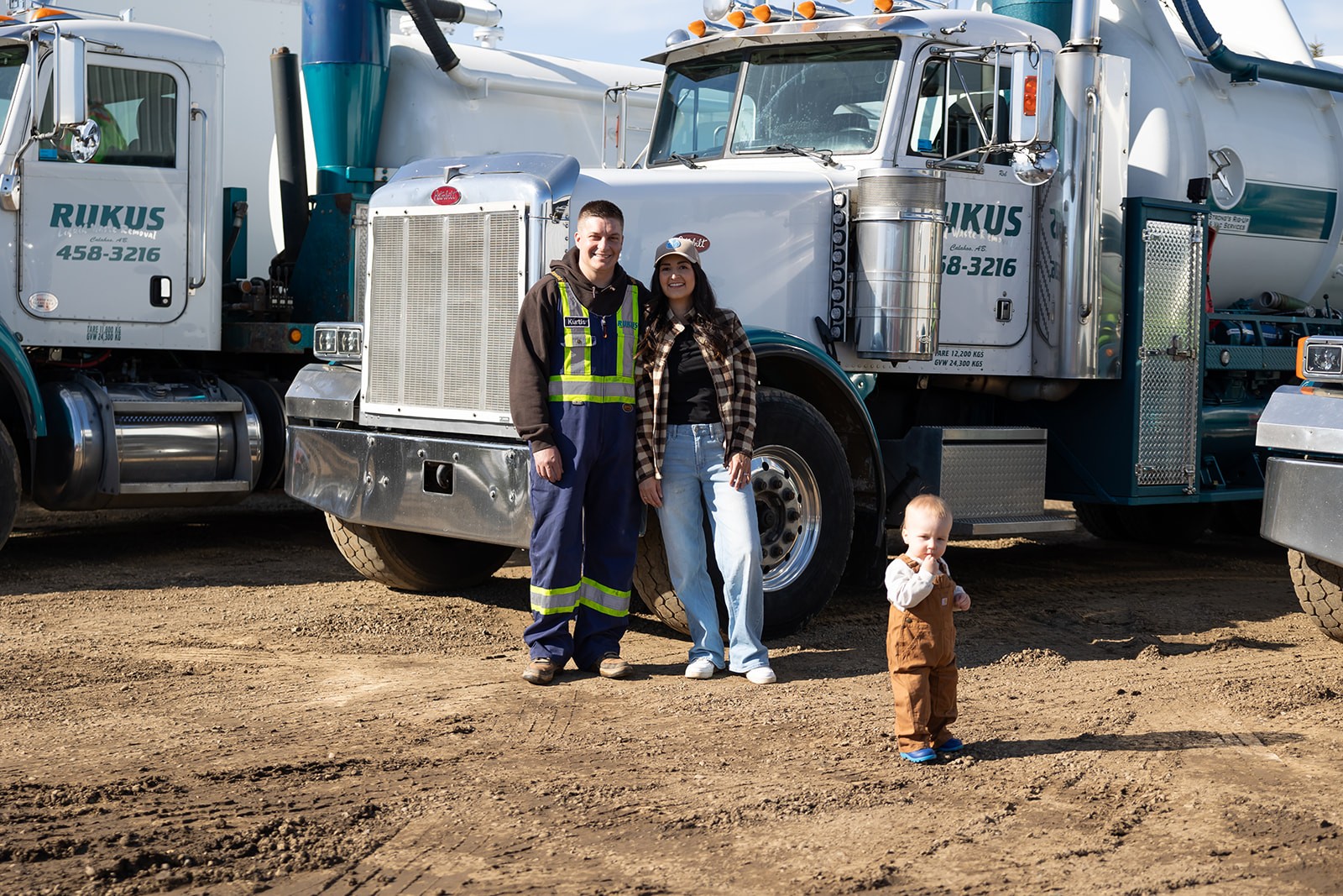 Family-owned Rukus Liquid Waste Removal with owners Kurtis and Bri Lozinski and their son in front of company vacuum trucks, showcasing septic and liquid waste services in Edmonton and surrounding Alberta communities