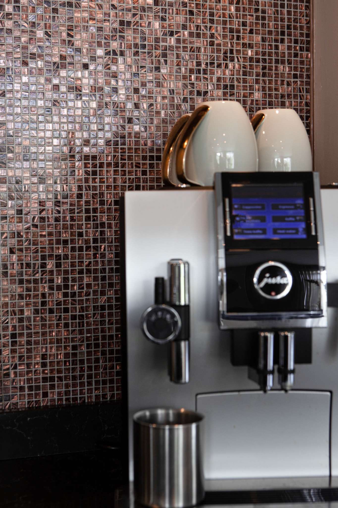 Detail van luxe koffiecorner met koperkleurige mozaïektegels en koffiemachine.