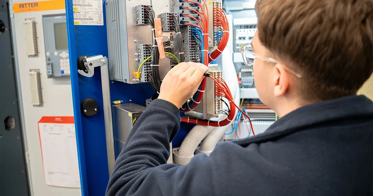Ein Mitarbeiter von RITTER Starkstromtechnik prüft die Verdrahtung und elektrische Komponenten in einem geöffneten Schaltschrank. Er führt eine Kontrolle der Elektroanlage im Produktionsbereich durch.