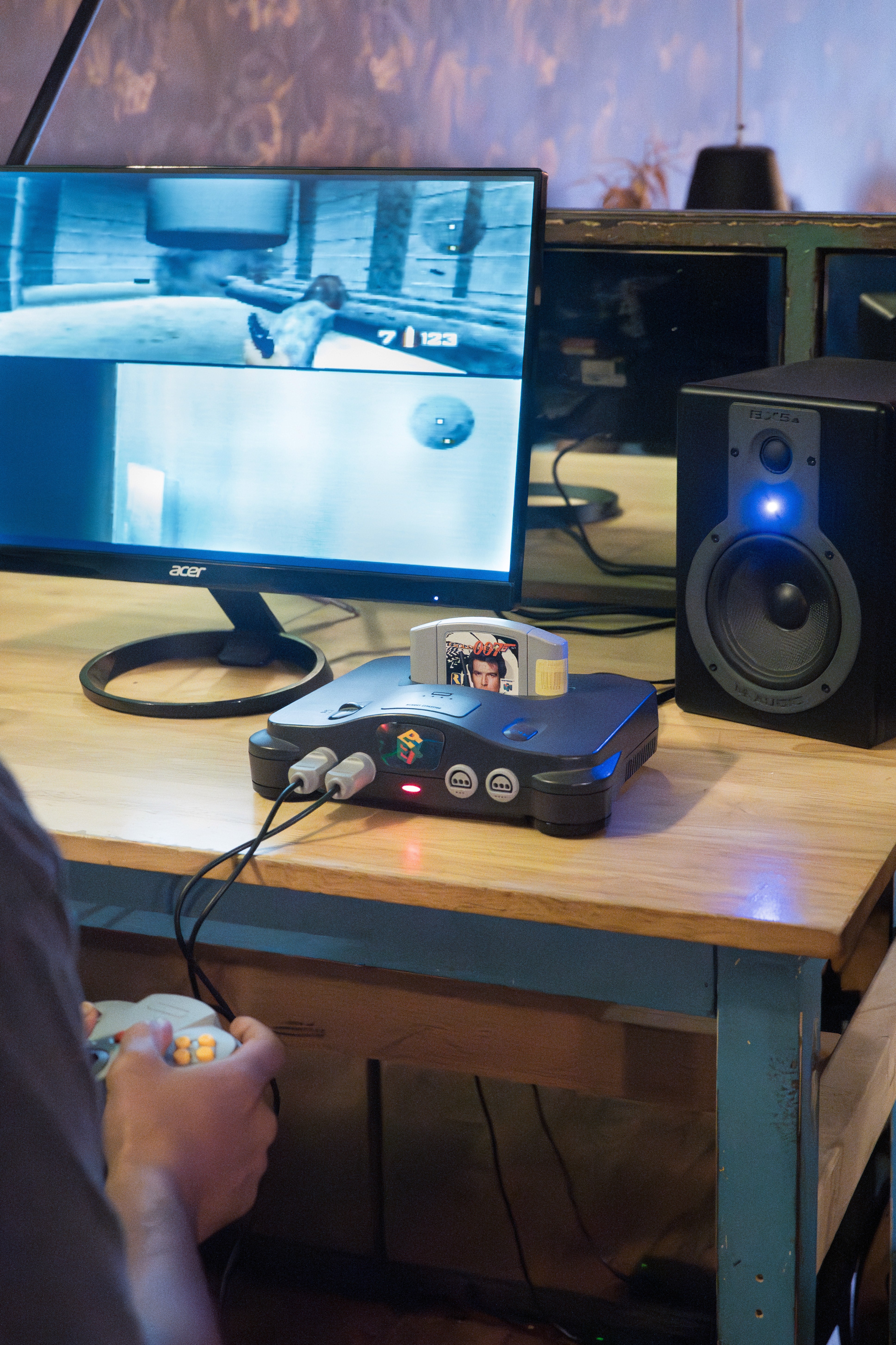 Nintendo 64 console on a desk with a 007 game cartridge inserted, monitor on, and studio speaker beside it.