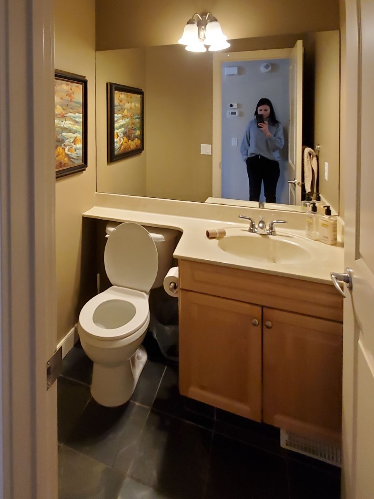 A small powder room with maple vanity and dark slate floors.