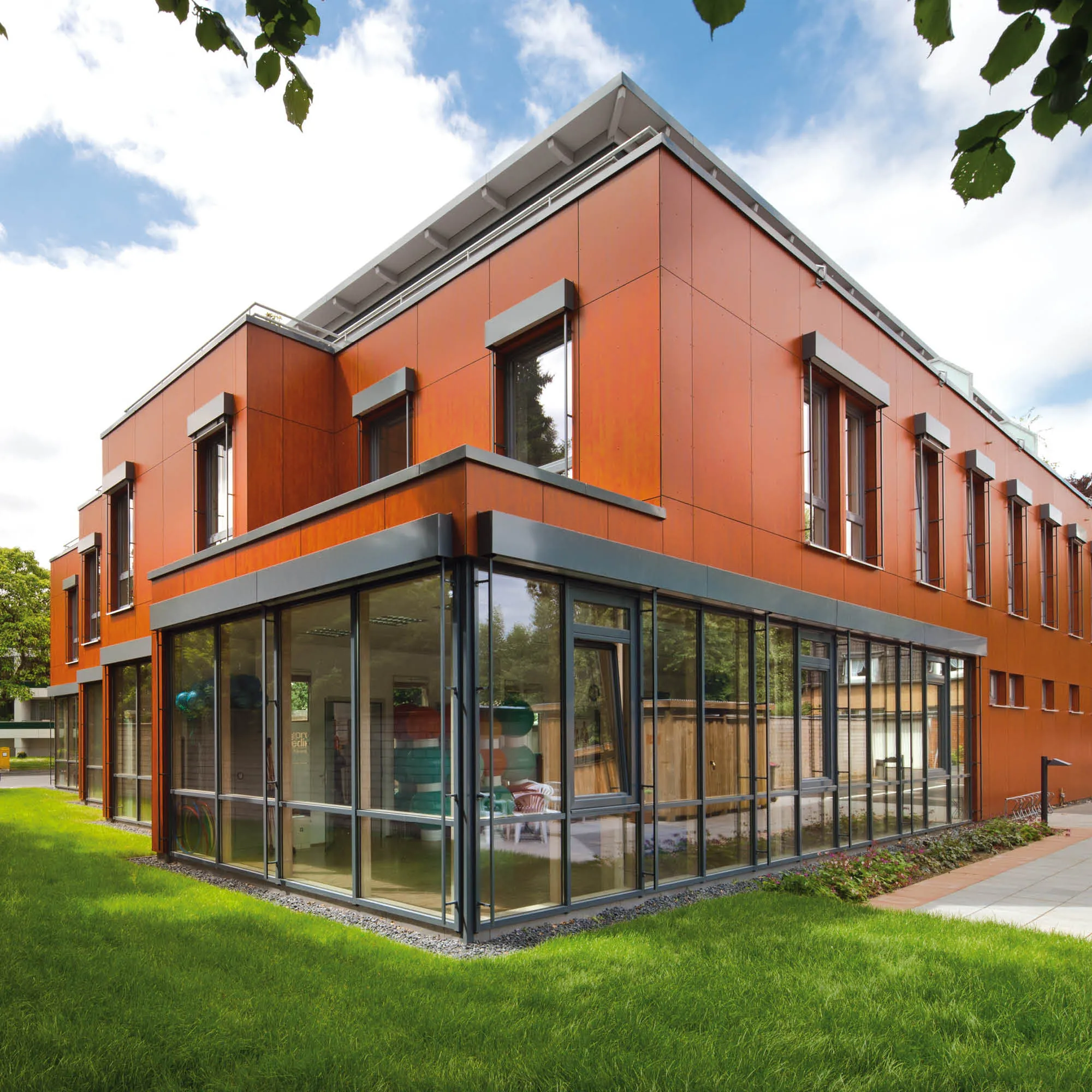 Modernes Gebäude mit orangefarbener Holzfassade, Glasfront und gepflegtem Rasen.