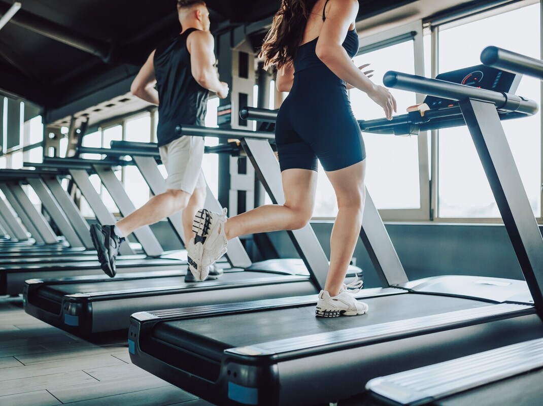 couple running on treadmills in the gym instead of working out on an elliptical to lose weight