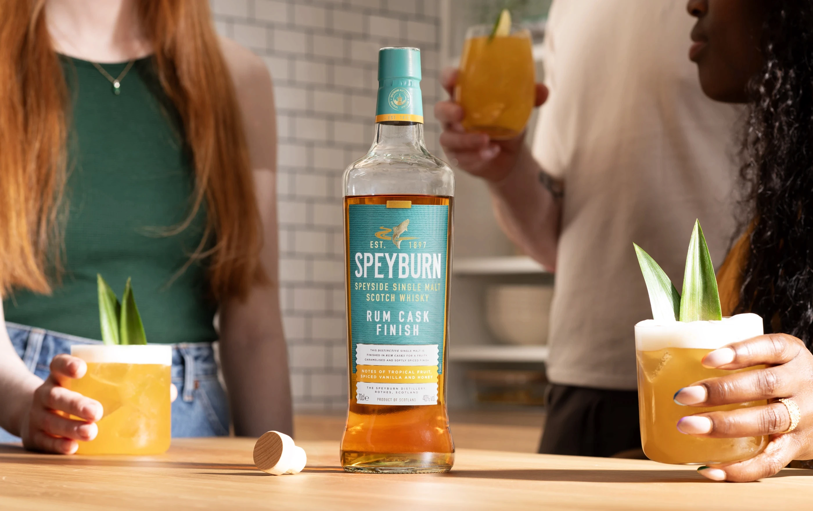 3 people enjoying cocktails with a bottle of Speyburn Whisky Rum Cask Finish as a focal point