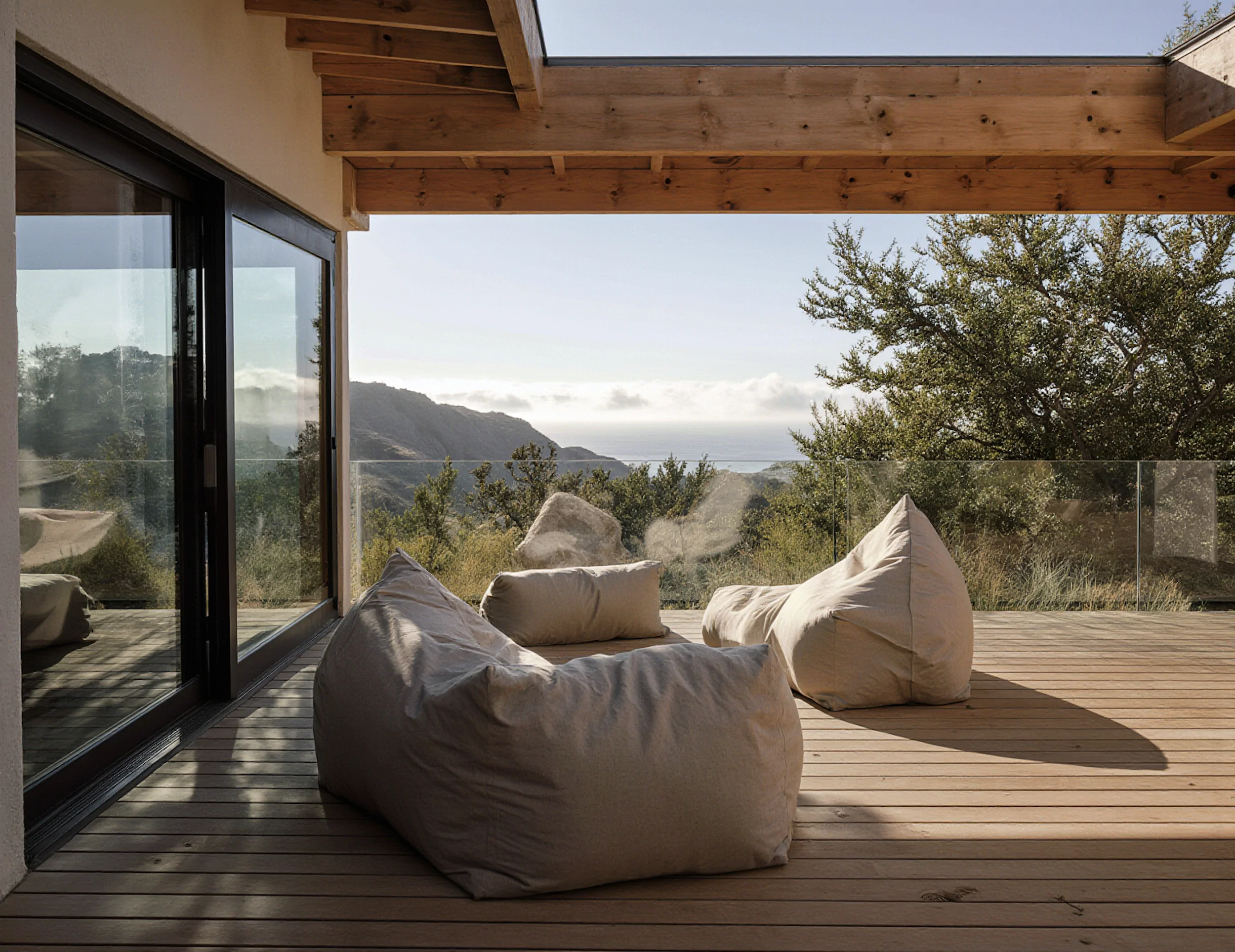 Outdoor deck with linen loungers overlooking rolling coastal terrain through floor-to-ceiling glass.