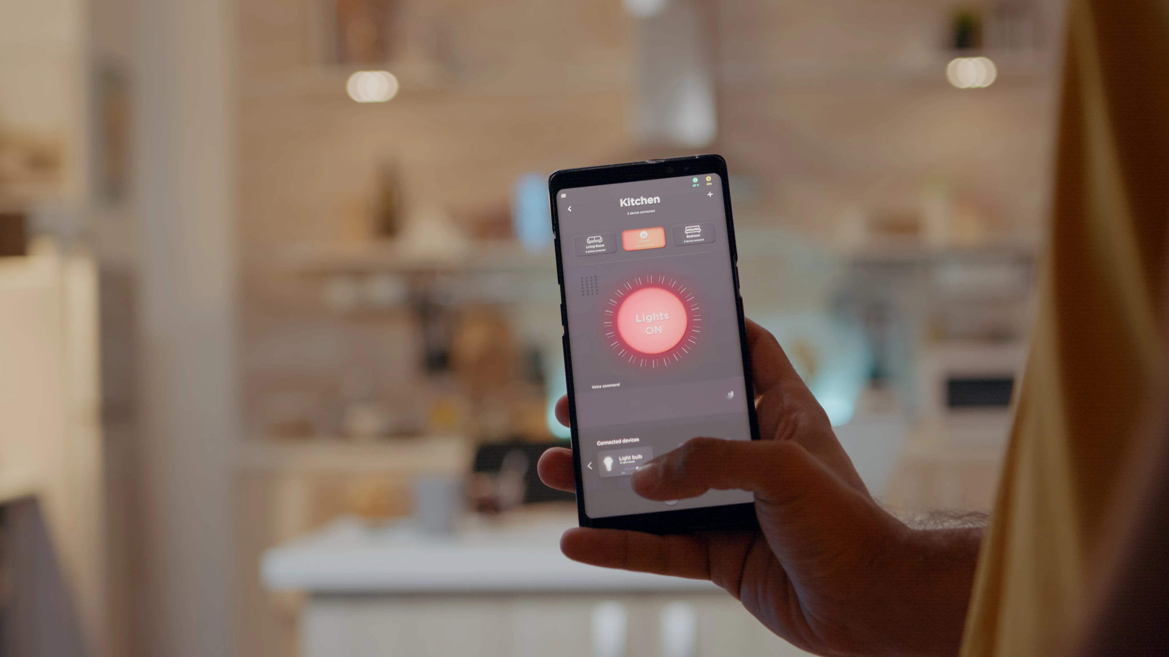 Close-up of a hand holding a smartphone displaying a red interface in a brightly lit room.