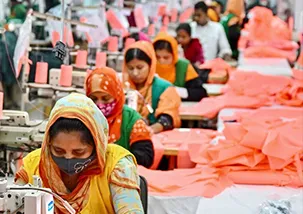 A garment production factory stitching floor where employees are working with their sewing machine. A sewing line where all the people are sitting one behind another with their sewing machine & fabrics on their side 