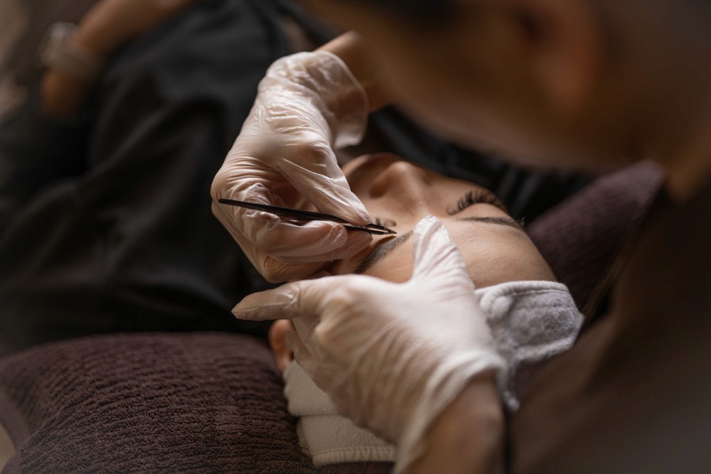 Close-up portrait of a person wearing a gray insulated hooded jacket with the hood up, showing their face framed by the hood against a light background.