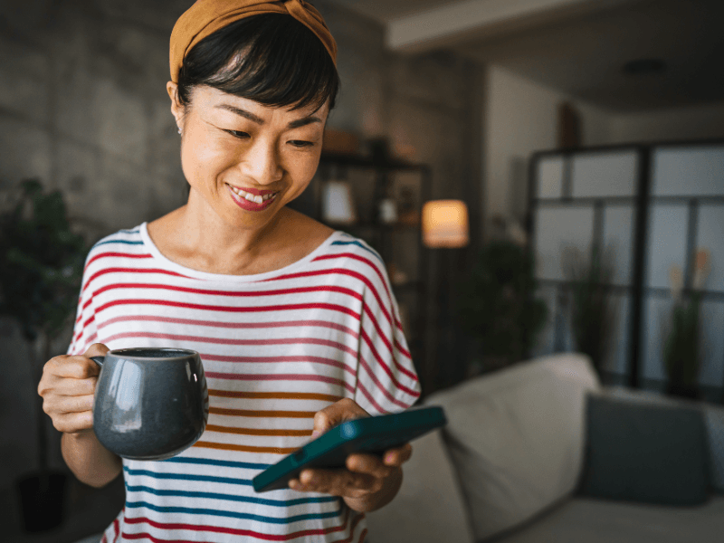 Asian woman looking at her cell phone while holding a mug