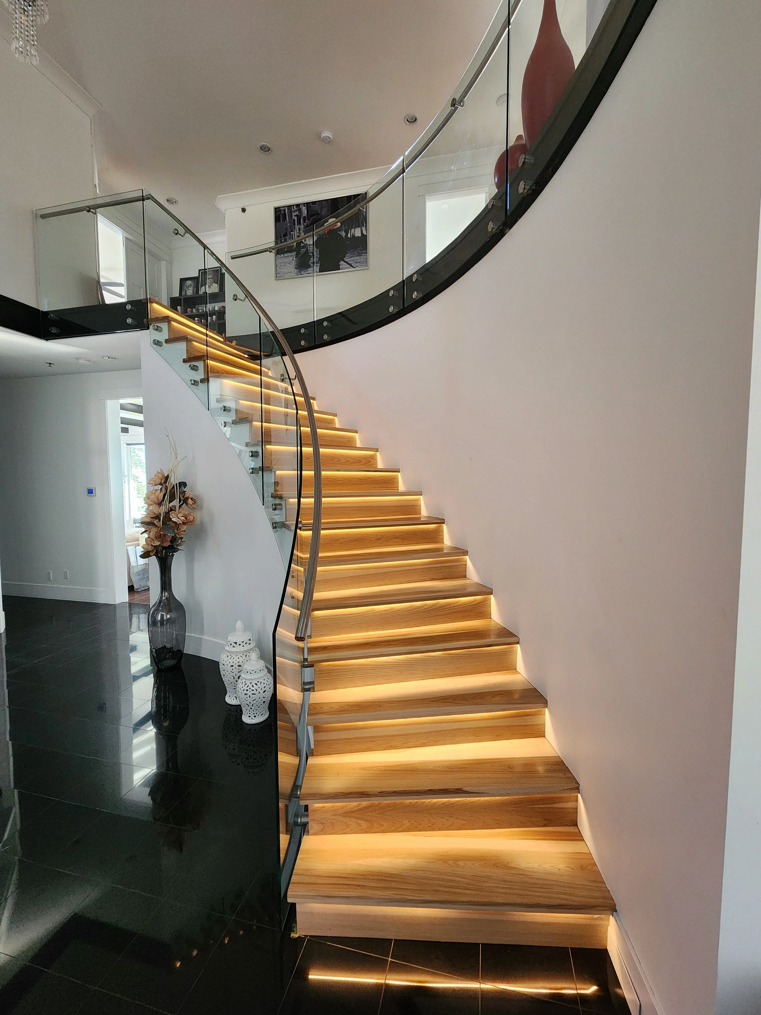 Curved interior staircase with 12mm glass railing panels, stainless handrail, and lit wood treads by Tenmar