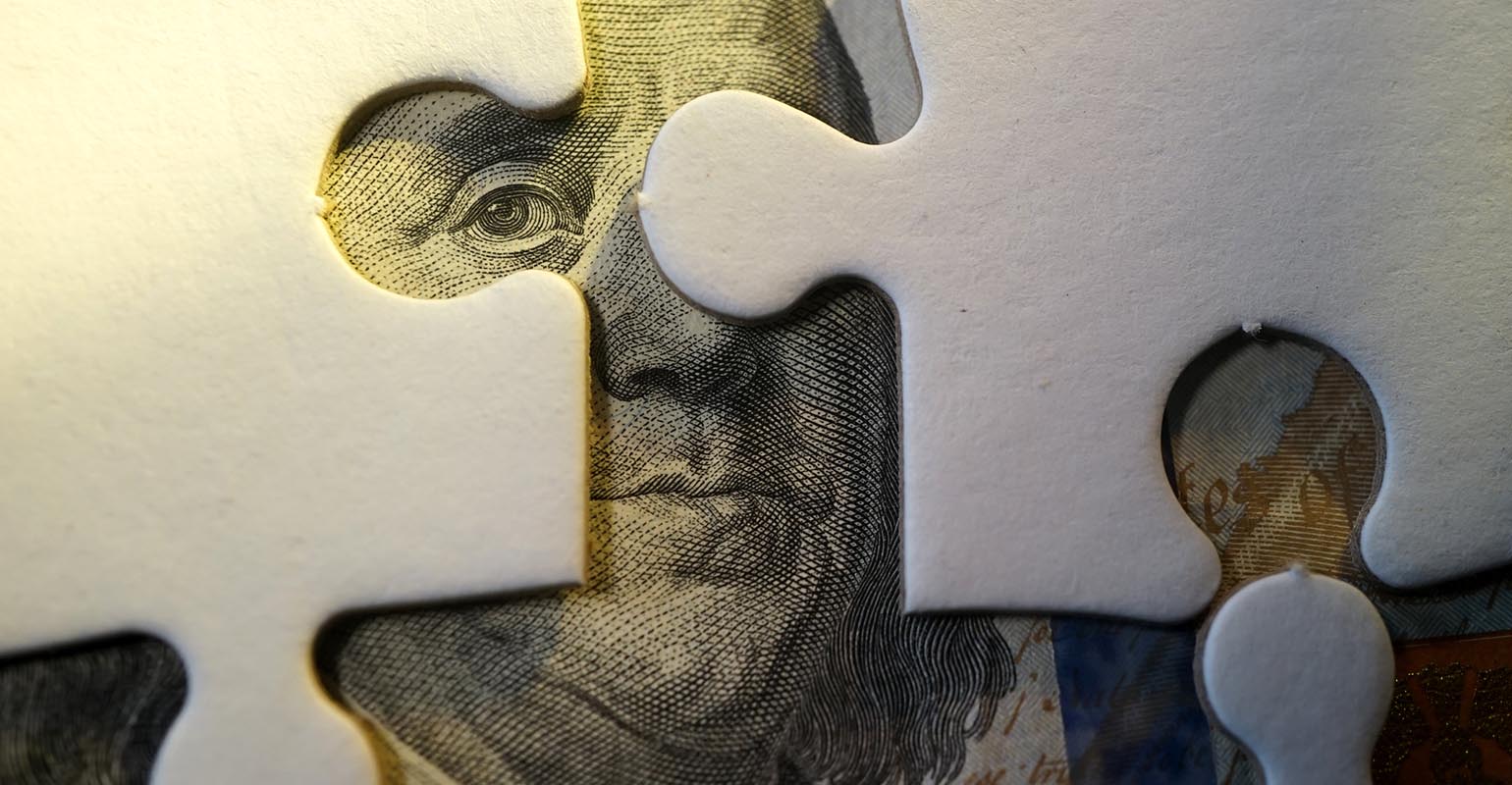 A dollar bill concealed by puzzle pieces, representing the pieces of the retirement ecosystem
