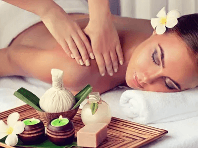 A woman receiving a massage with spa products and floral accents on a wooden tray nearby.