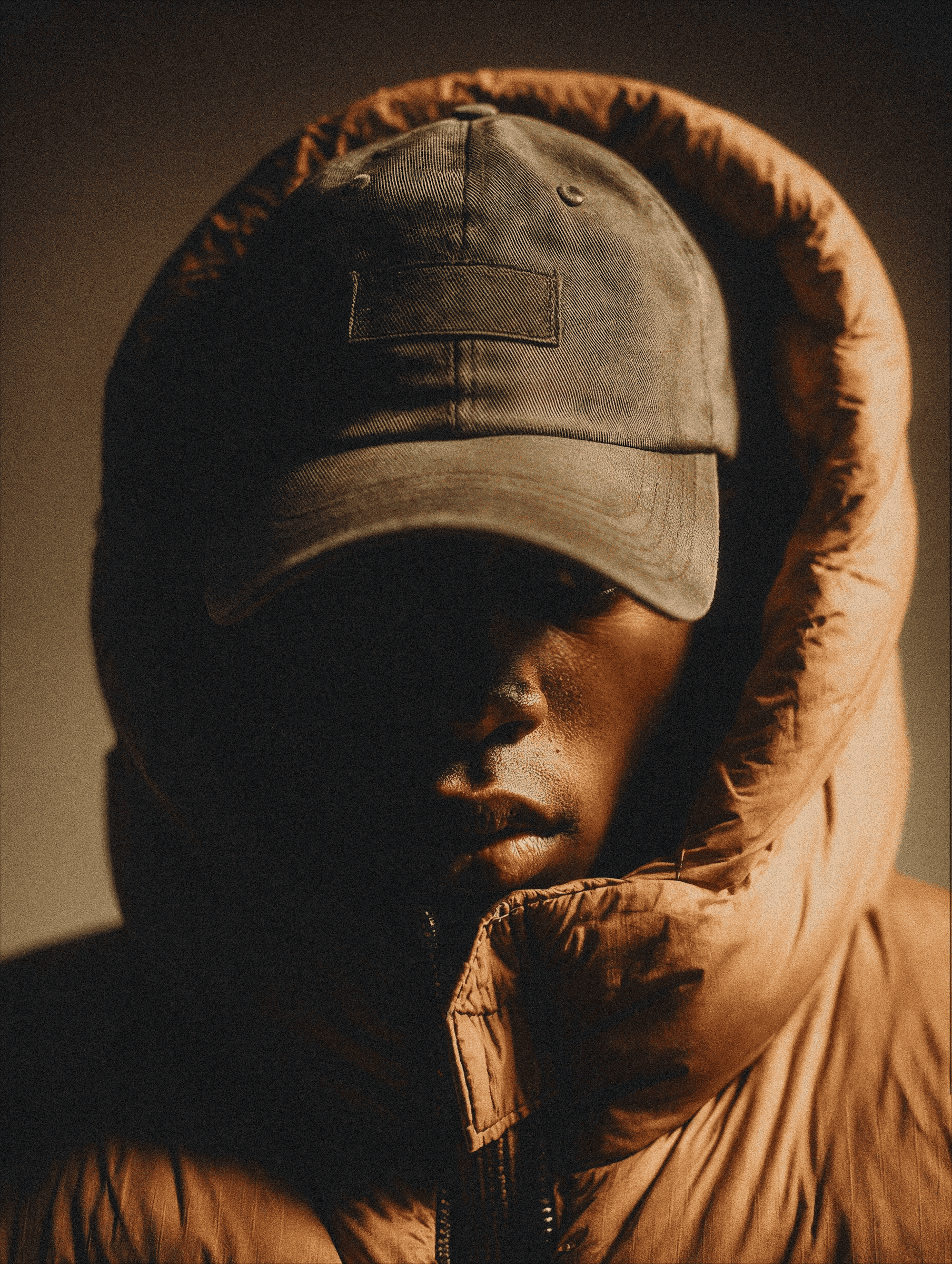 Man wearing a brown puffer jacket and cap looking to the side in warm lighting