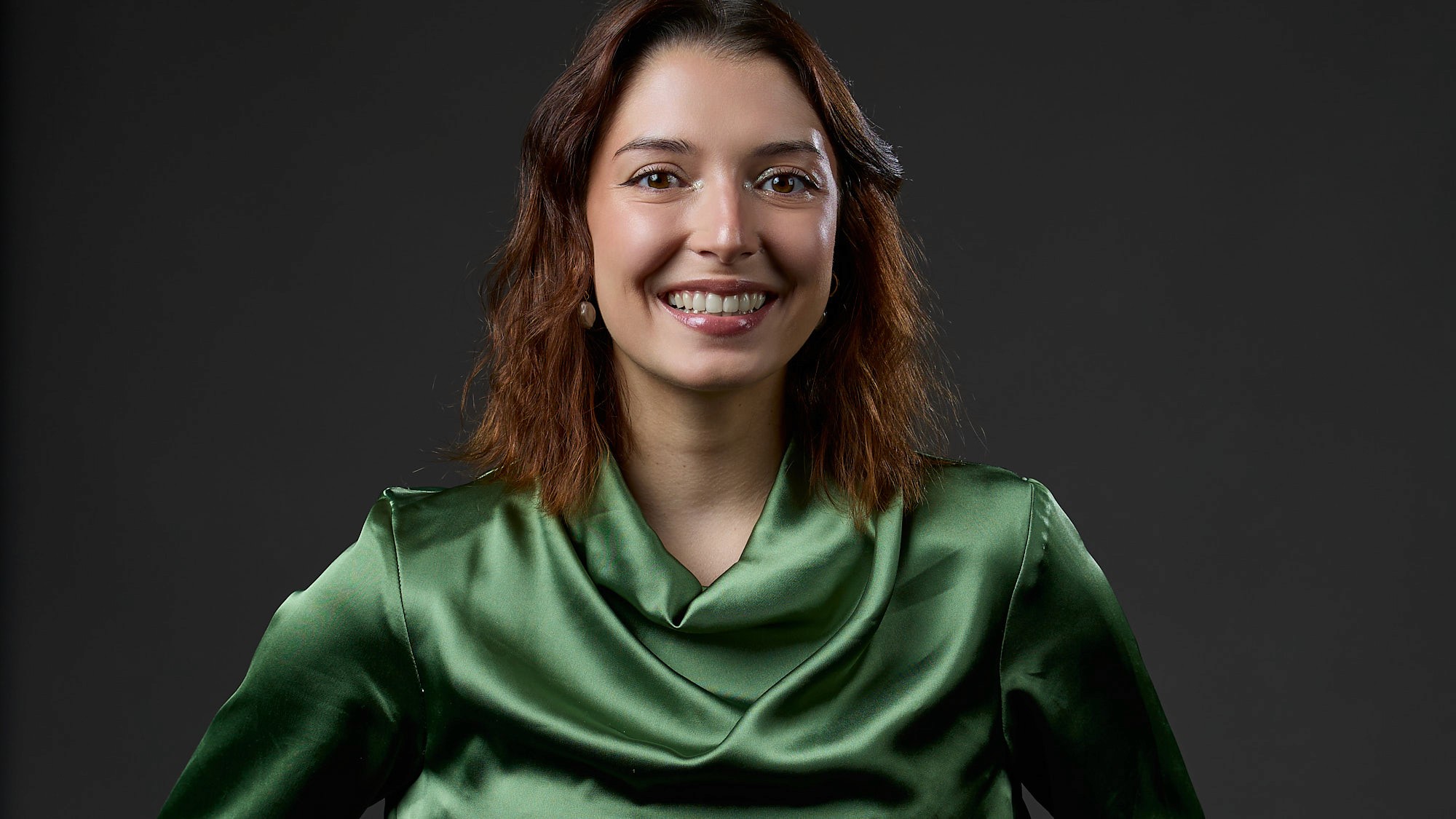 Portrait d'une femme graphiste avec un haut vert chic, sur fond gris foncé