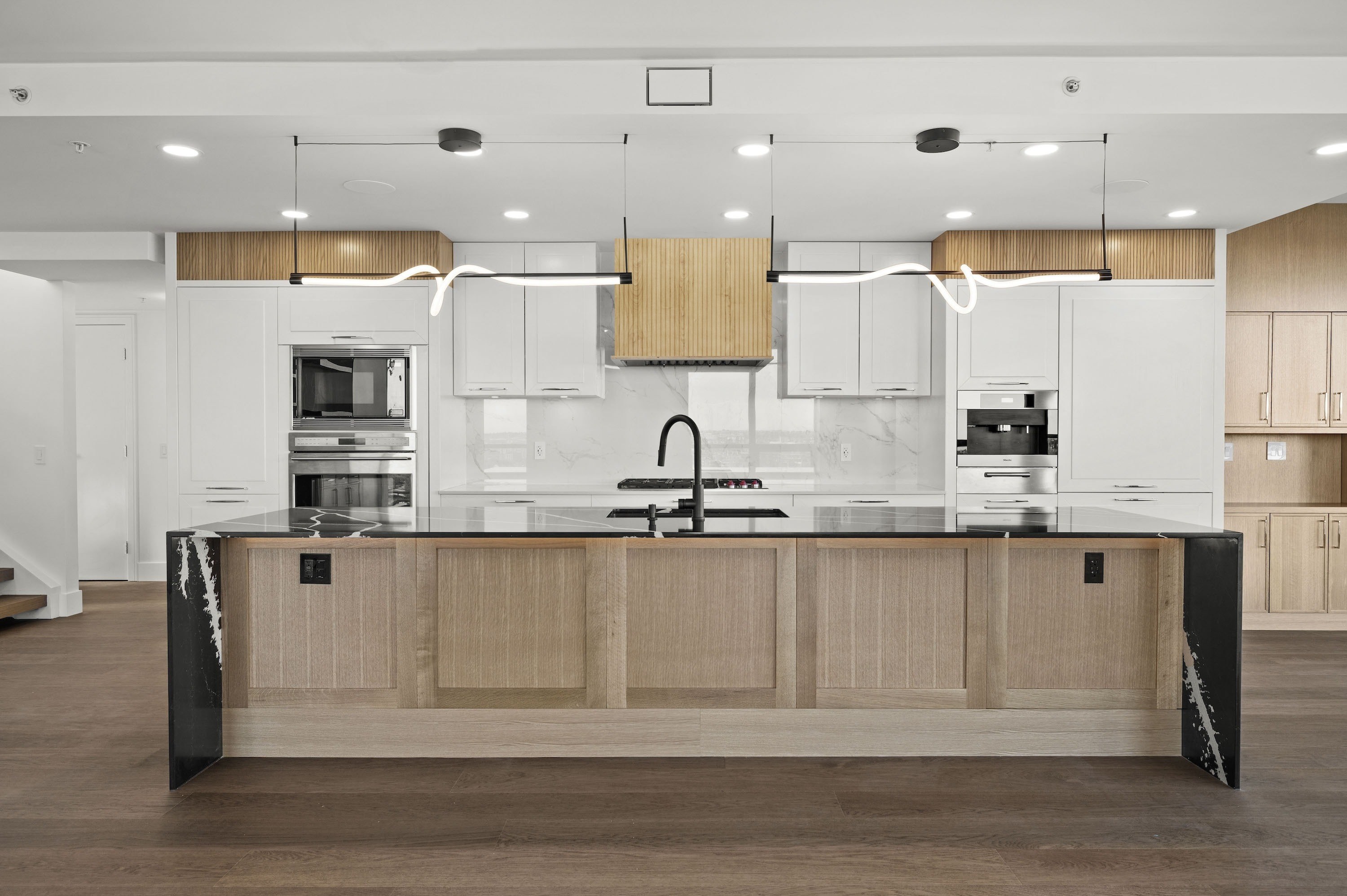 Eau Claire kitchen after: white and oak cabinetry, fluted oak range hood, black marble waterfall island and sculptural pendants