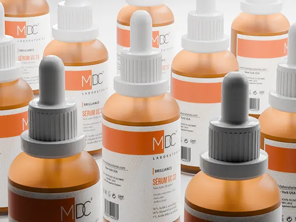 Multiple bottles of MDC Laboratories' 'Brilliance Serum VC 33,' featuring orange labels with white text and dropper caps, arranged on a surface in a clean, organized display