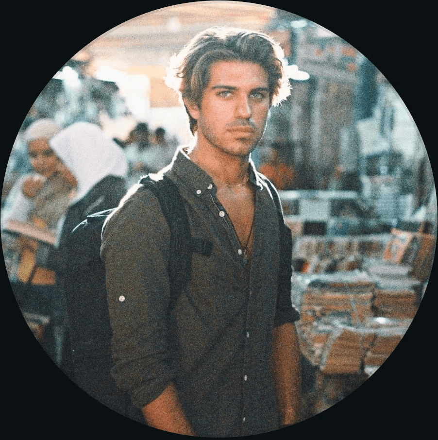 Young man with curly hair and beard smiling in sunlight.