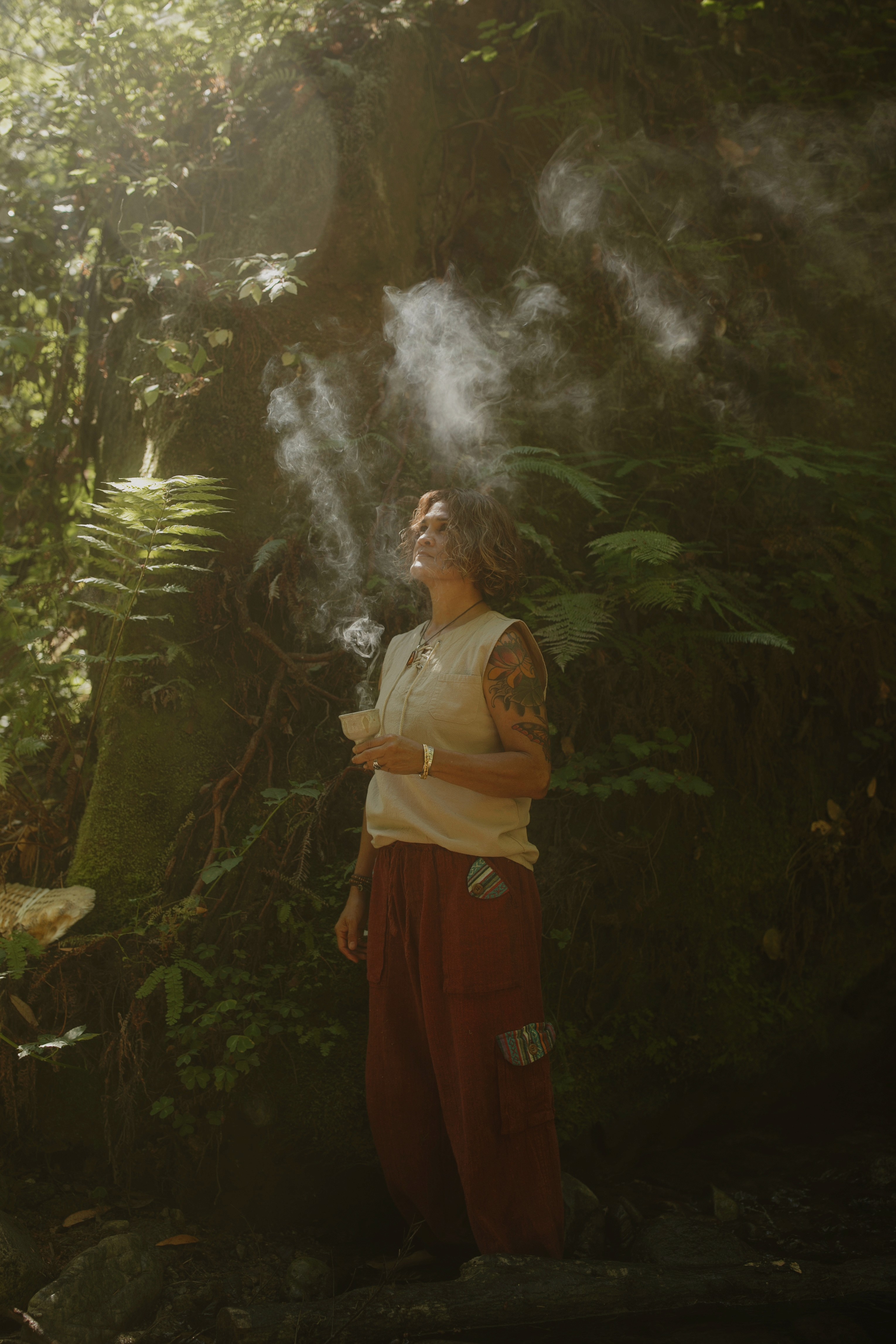 Sonia performing a smoke cleansing ritual in a sunlit jungle during a sacred plant medicine ceremony