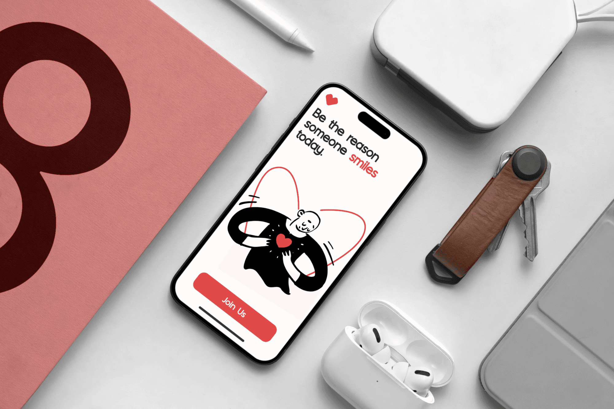 A smartphone displaying a motivational message with an illustration, surrounded by tech accessories like AirPods, a leather key holder, and a square notepad, on a minimalistic desk setup.