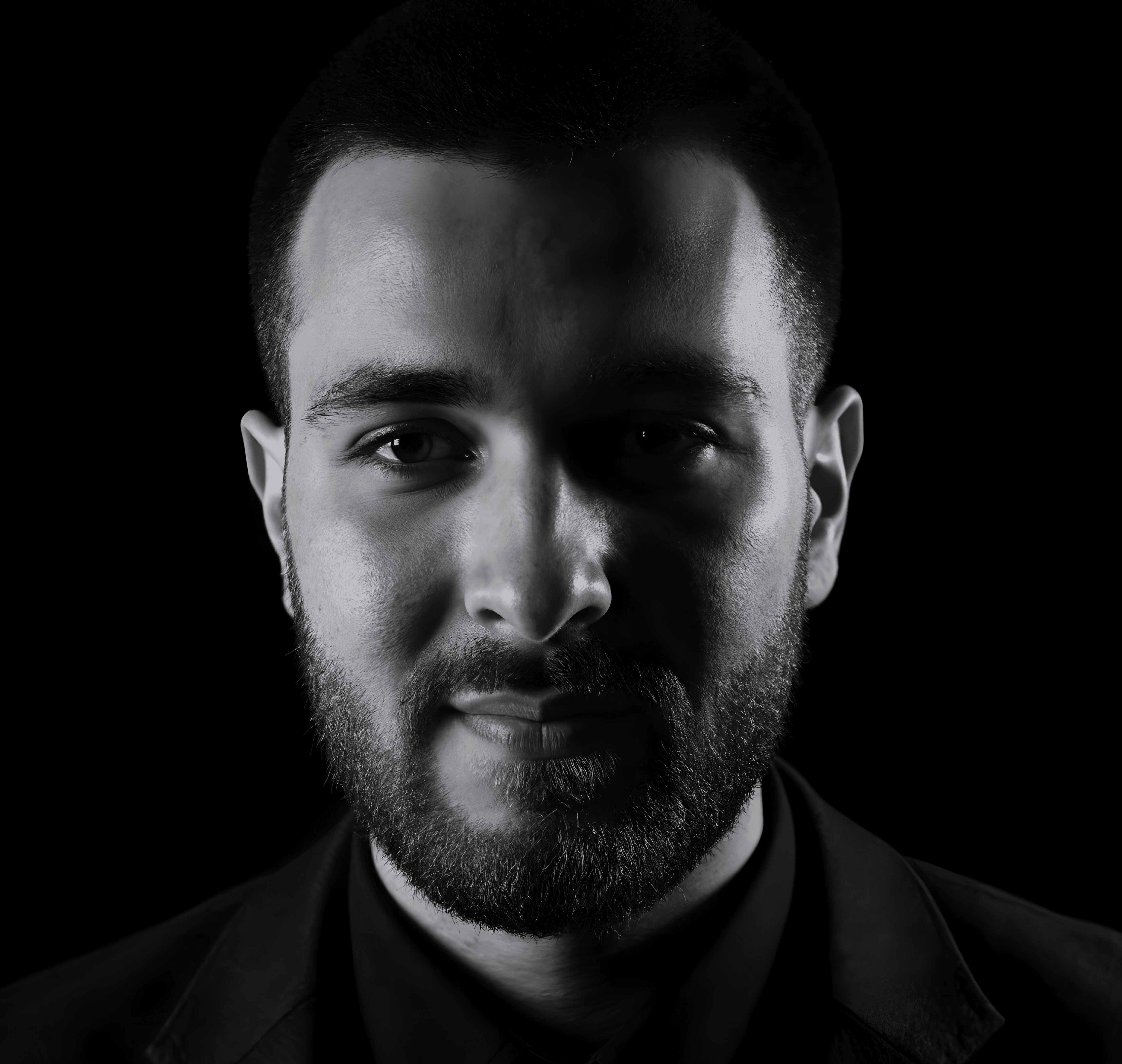 Portrait of a young man with short hair, wearing a dark t-shirt, against a plain background.