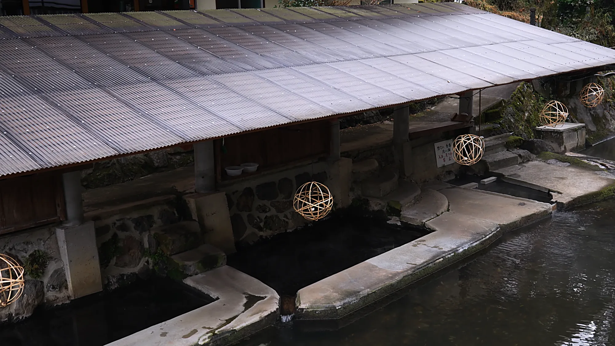 A metal-roofed riverside shelter at Kurokawa Onsen with lantern spheres hung beneath it