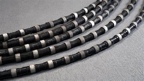 Multiple lengths of diamond wire saw coiled on a grey surface, each with visible metal cutting segments. These wires are designed for use in large-scale industrial cutting operations.