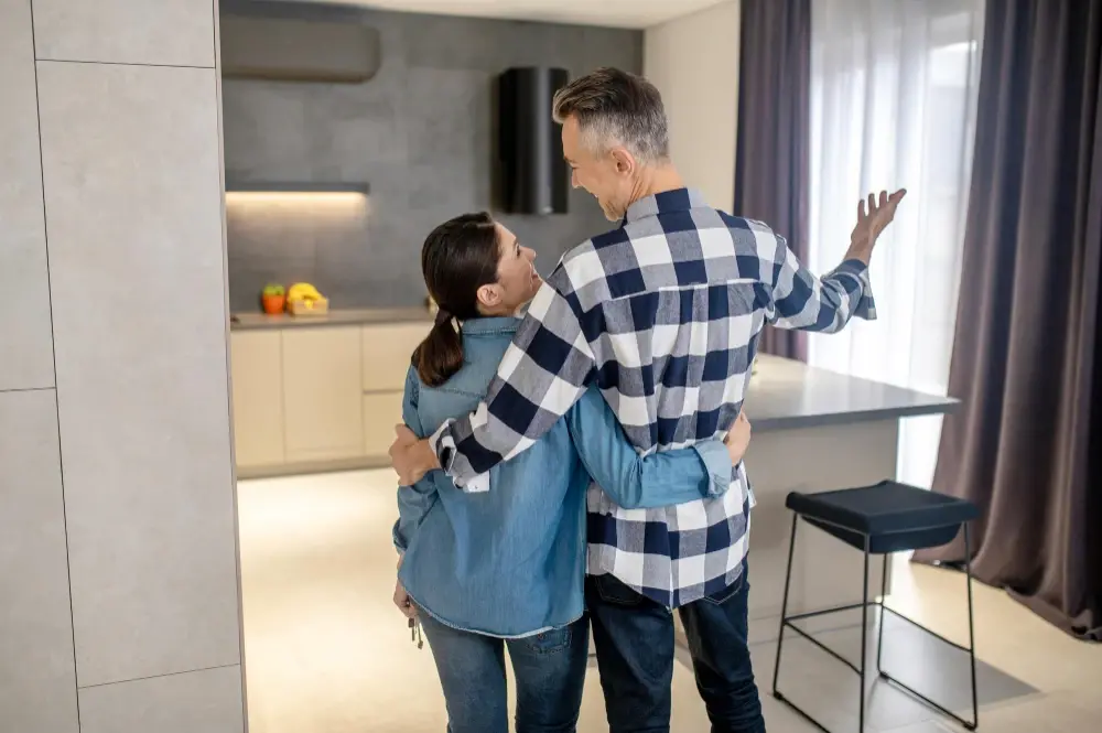 A happy couple stands in their new home, smiling as they admire the modern kitchen together. The moment captures the excitement and pride of new homeowners made possible through Chris Lewis Home Loans.