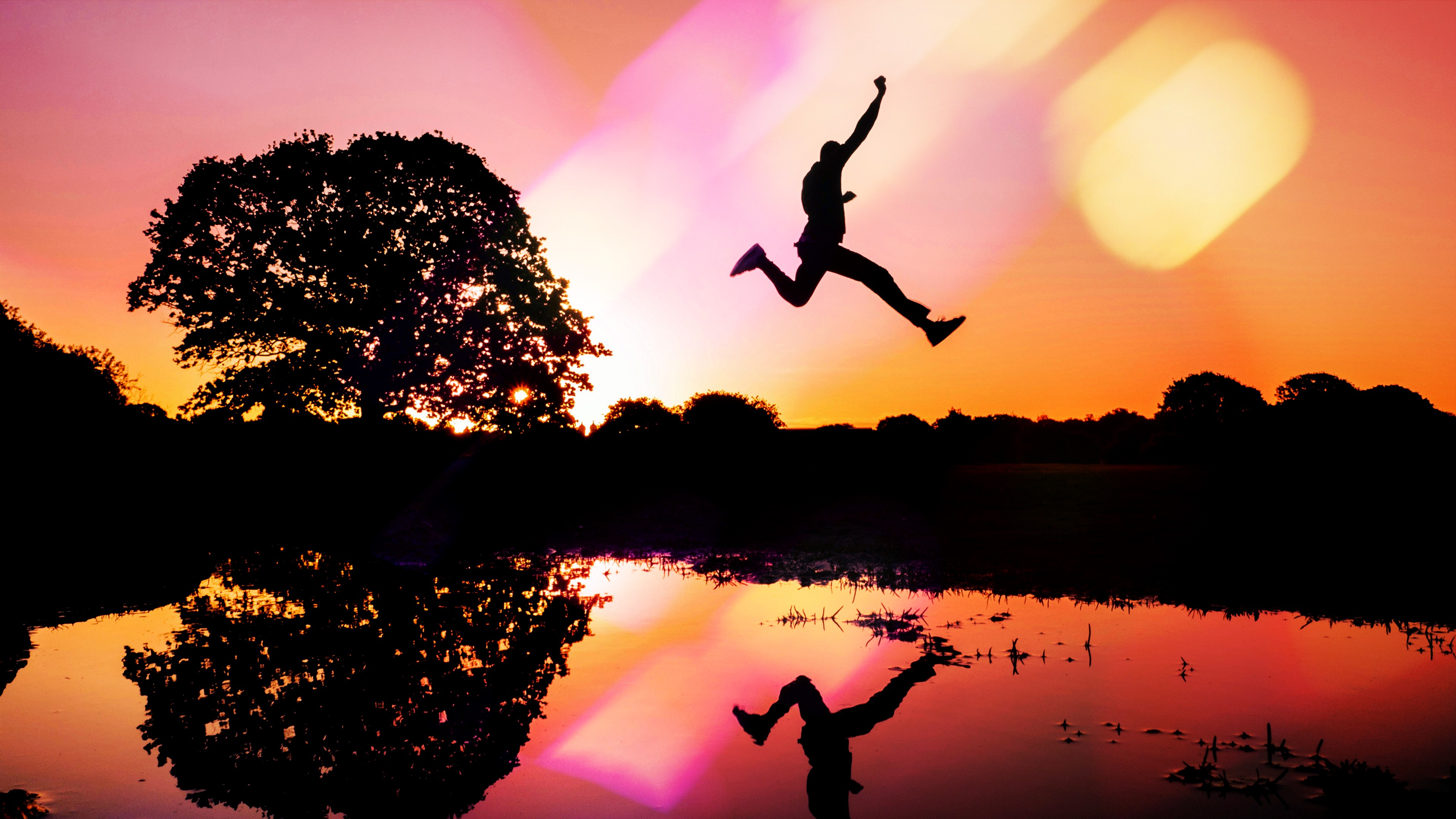 A silhouette of a person juming over a body of water at sunset