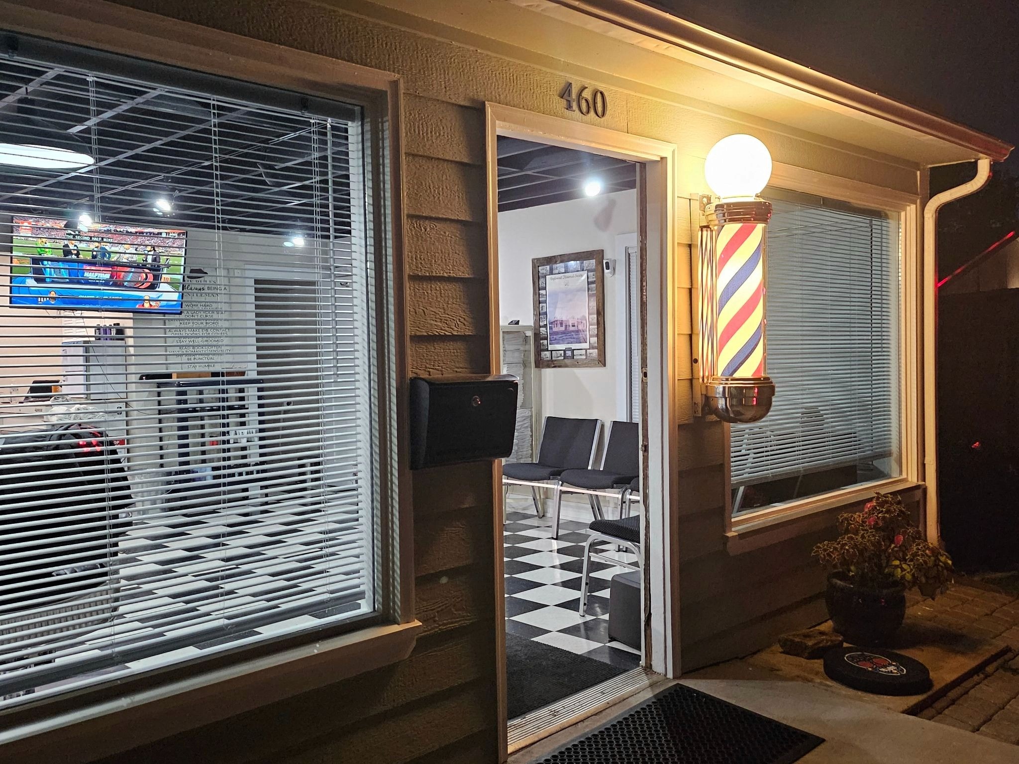 Nighttime view of Quincy Barbers storefront with vintage barber pole, open doorway, and welcoming interior visible.