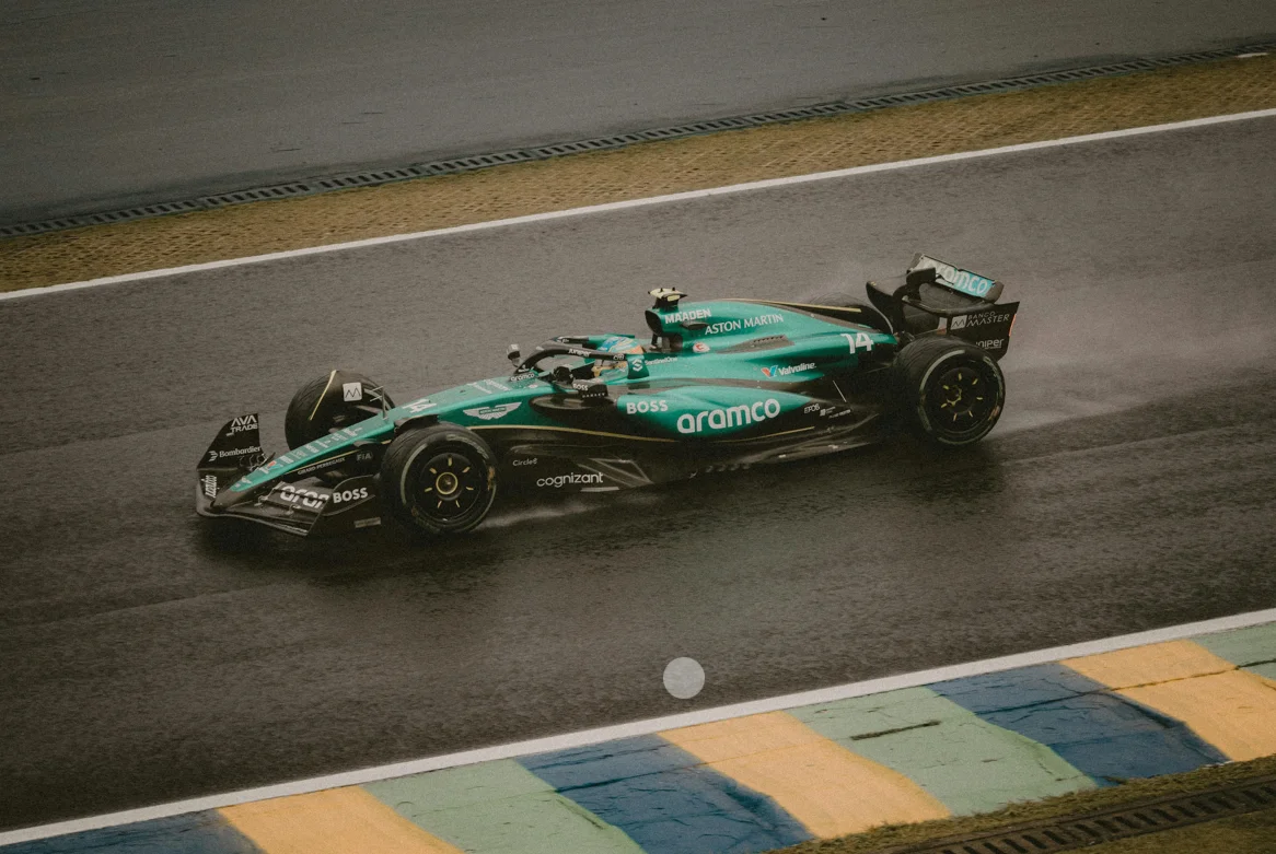 Une monoplace Aston Martin de Formule 1 lancée à pleine vitesse sur une piste détrempée. L’aérodynamique affûtée, les projections d’eau et la livrée verte iconique rappellent l’engagement historique de la marque dans la performance extrême et la compétition de haut niveau.