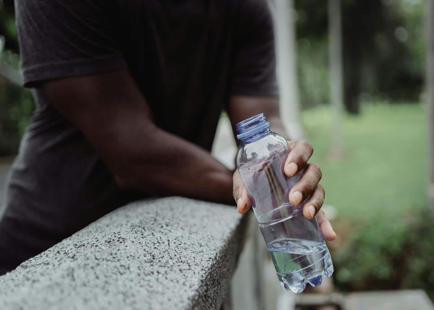 Person outdoors holding an open plastic water bottle
