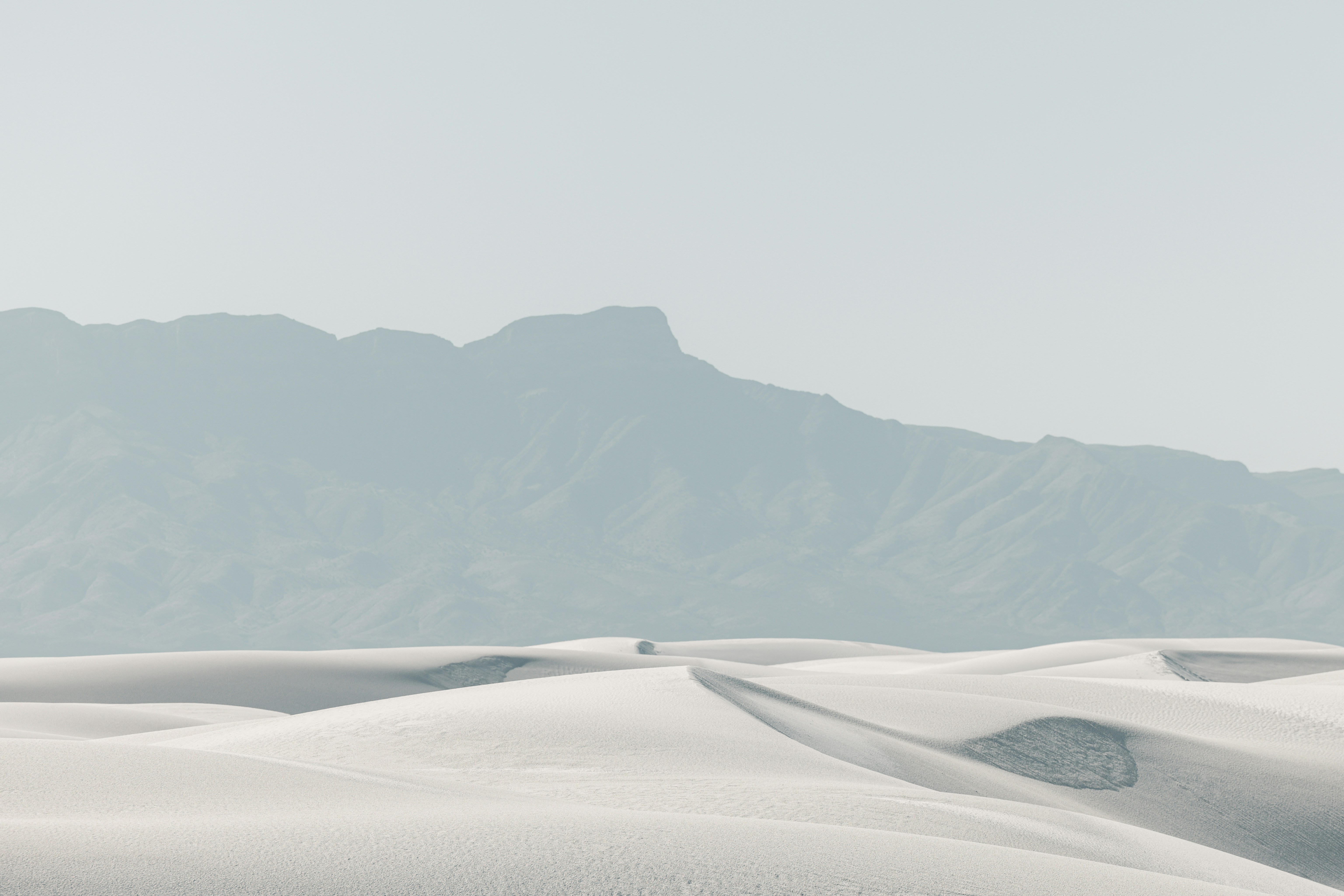 A lone vehicle drives across vast white sand dunes.