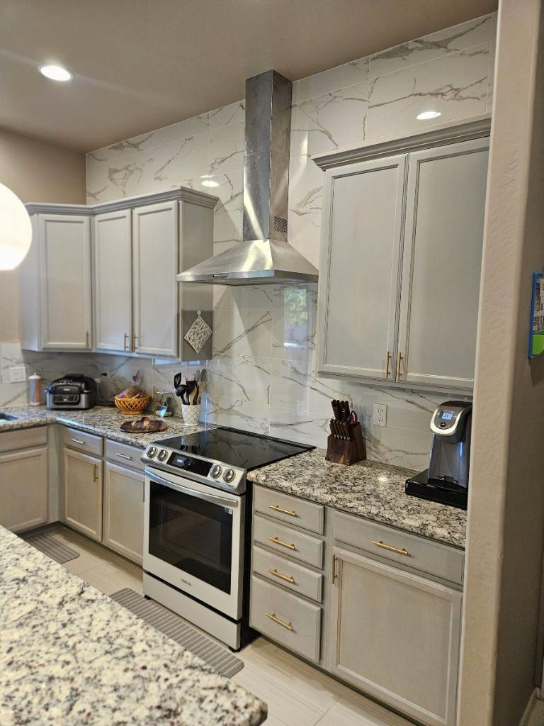 Modern kitchen with white cabinets, stainless steel range hood, and a marble tile backsplash above a stovetop and oven.