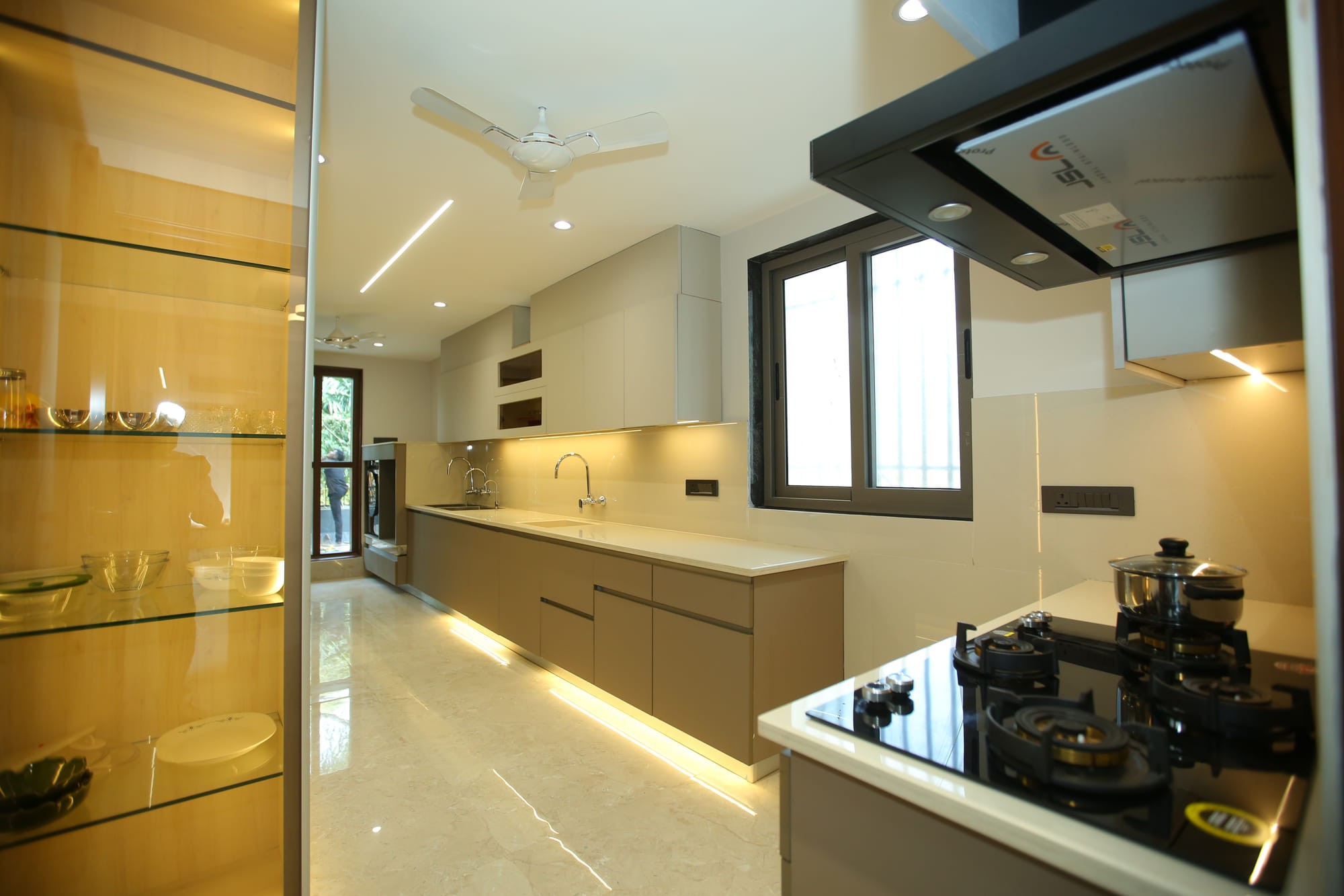 Handleless kitchen with a long stone worktop, gas hob and a glazed display unit