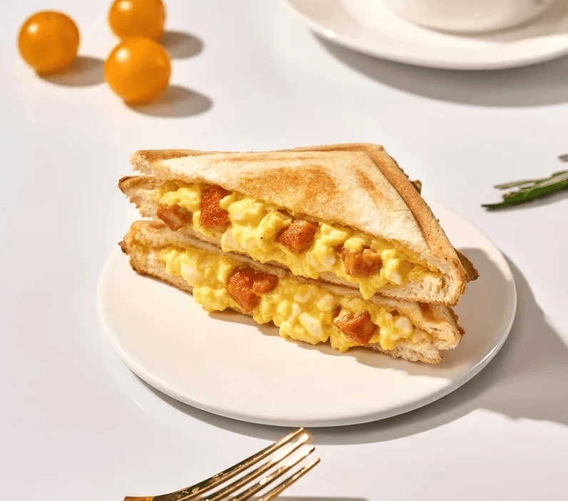 A delicious egg salad sandwich, rich in creamy yellow egg products and savory red diced ingredients, rests on a white.