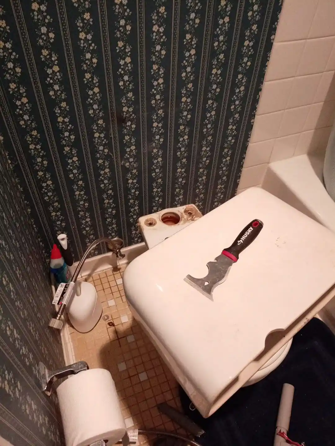 A removed porcelain toilet tank and scraper tool prepared during a professional toilet replacement.