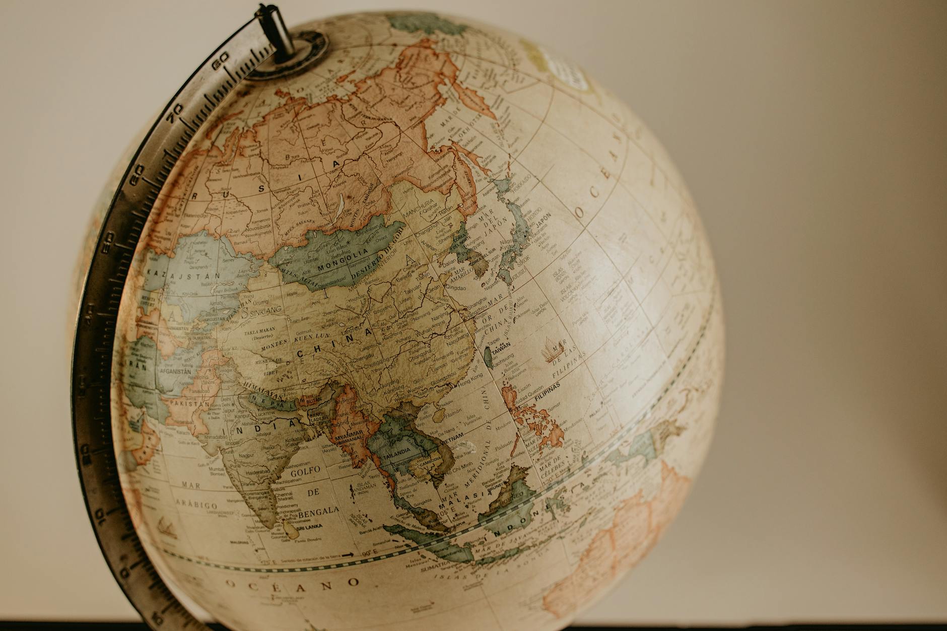 Two students pointing at a large physical globe while holding historical figure flashcards in a classroom.