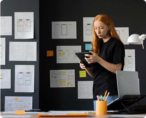 Person reviewing a tablet in a workspace with UX wireframes on the wall